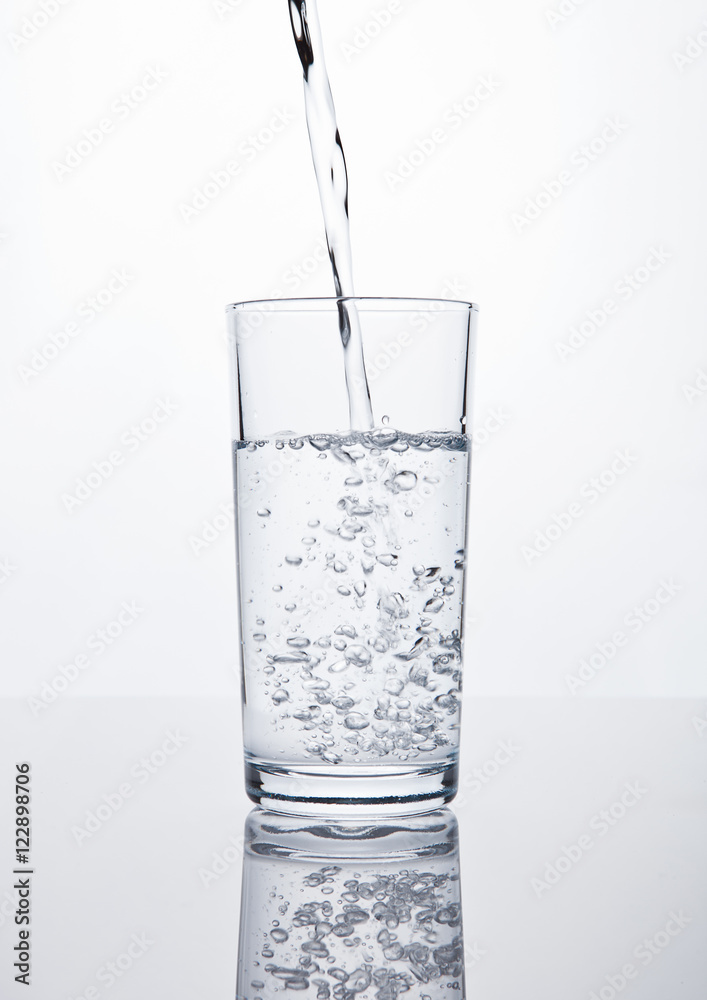 Pouring still clean water in glass on white Pouring still clean water in glass on white