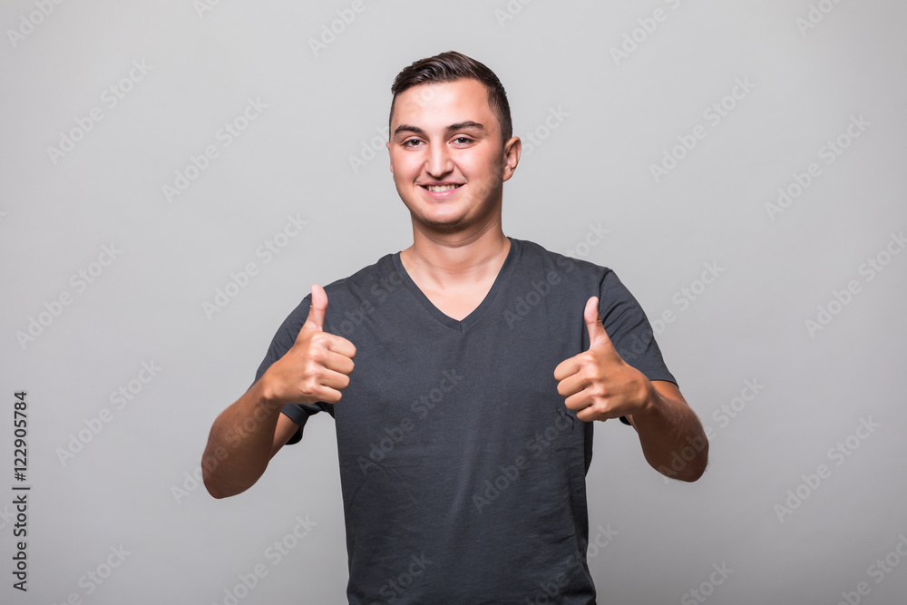 Portrait of a smiling casual man showing two thumbs up and looking at camera over gray background Portrait of a smiling casual man showing two thumbs up and looking at camera over gray background