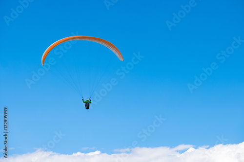 Paraglider gliding over white clouds in clear blue sky