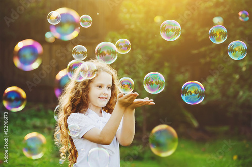 Funny little girl catching soap bubbles in the summer on nature.