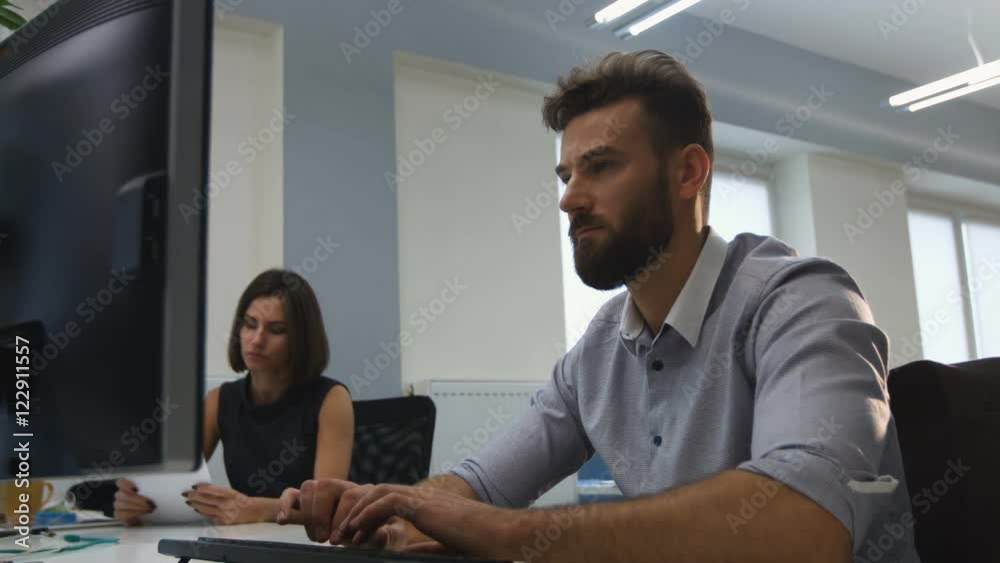 Office worker using his laptop , while his colleaugues check documents. Office worker using his laptop , while his colleaugues check documents.
