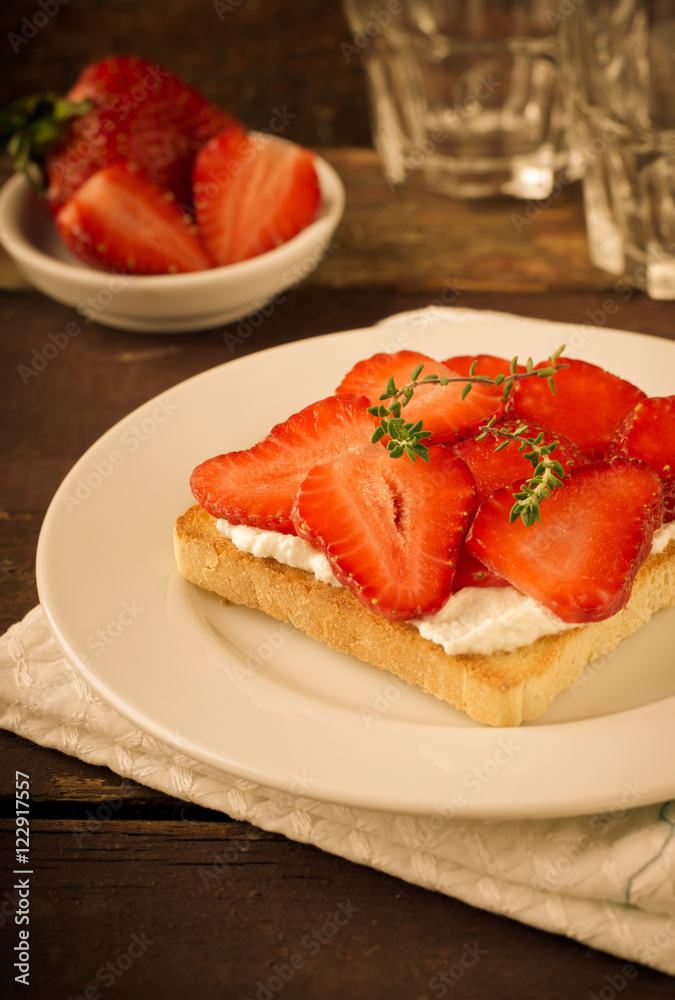 Toasted bread with cream cheese, strawberries and thyme on wooden table