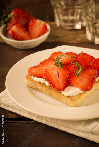 Toasted bread with cream cheese, strawberries and thyme on wooden table