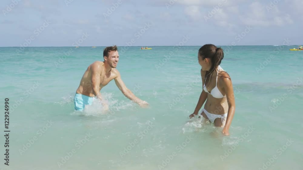 Lifestyle people fun - beach couple splashing water playing together laughing on vacation. Young happy multicultural woman and man playful enjoying turquoise water and blue sky. RED EPIC SLOW MOTION. Lifestyle people fun - beach couple splashing water playing together laughing on vacation. Young happy multicultural woman and man playful enjoying turquoise water and blue sky. RED EPIC SLOW MOTION.