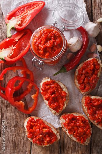 Ajvar in a glass jar and toast on a wooden background. Vertical top view
