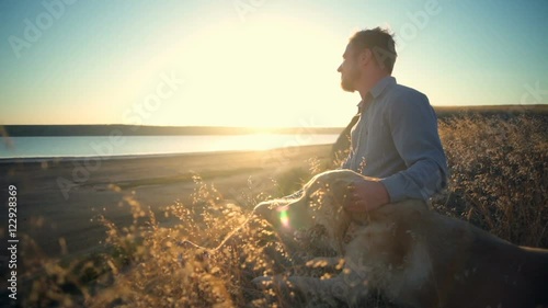 smiling man and dog sitting at the edge of cliff at sunset