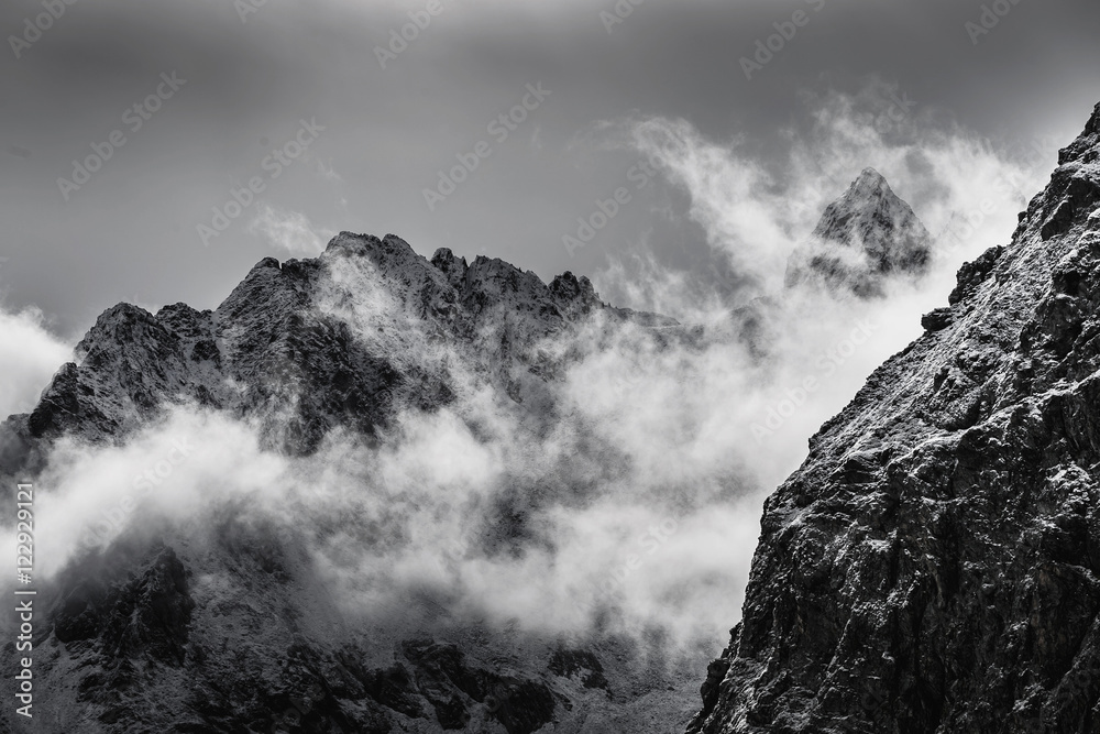 black and white photo of snow covered rocky mountain peaks with fog