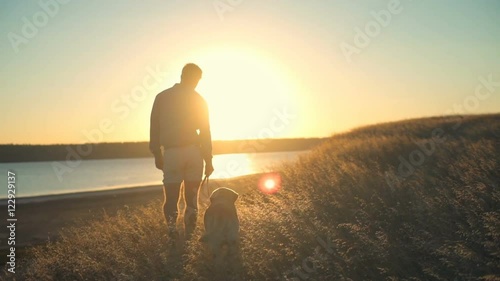 back view of man walking with dog along the edge of cliff at sunset
