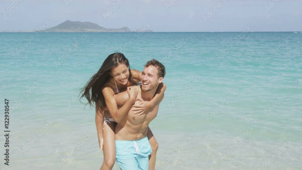 Beach couple vacation fun - happy piggyback. Cute mixed race asian chinese woman piggybacking on the back of handsome caucasian man laughing in love during summer holidays or vacations. Beach couple vacation fun - happy piggyback. Cute mixed race asian chinese woman piggybacking on the back of handsome caucasian man laughing in love during summer holidays or vacations.