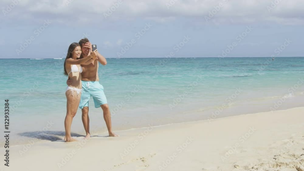 Self portrait couple taking selfie with smartphone on beach on travel vacation holidays. Young Asian woman and Caucasian man using mobile cell smart phone camera taking photos. RED EPIC. 96 FPS. Self portrait couple taking selfie with smartphone on beach on travel vacation holidays. Young Asian woman and Caucasian man using mobile cell smart phone camera taking photos. RED EPIC. 96 FPS.