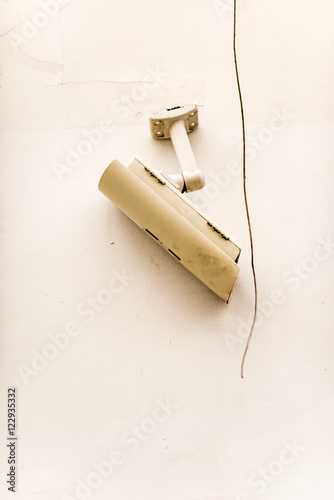 Broken surveillance camera on white wall