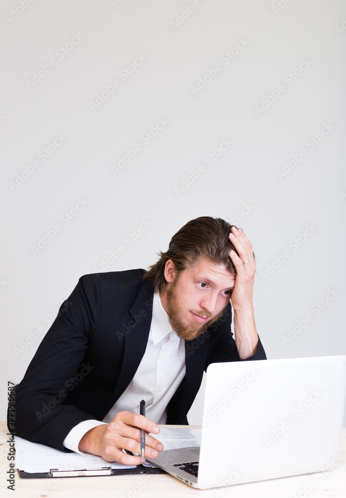 sad exhausted young business man sitting at working desk with laptop and having work troubles in office sad exhausted young business man sitting at working desk with laptop and having work troubles in office