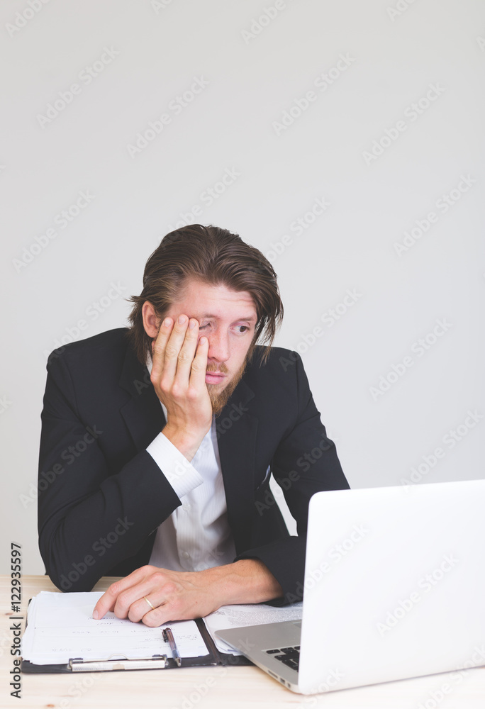 Thoughtful bearded young man experiencing troubles and looking very tired at company office Thoughtful bearded young man experiencing troubles and looking very tired at company office
