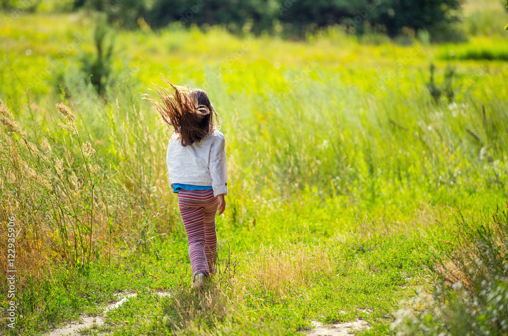Little girl running on the dirt rural road in the field