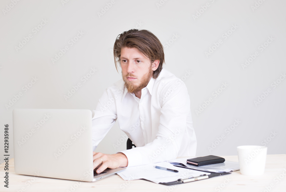serious young bearded man in formalwear working with laptop at company office serious young bearded man in formalwear working with laptop at company office