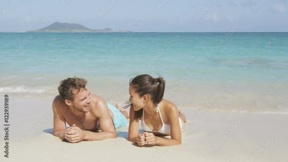 Couple in love relaxing on beach during vacation travel. Happy couple portrait talking together in a happy relationship sun tanning lying on the sand having fun in Hawaii, United States of America. Couple in love relaxing on beach during vacation travel. Happy couple portrait talking together in a happy relationship sun tanning lying on the sand having fun in Hawaii, United States of America.