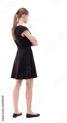 back view of standing young beautiful woman. girl watching. Rear view people collection. backside view of person. Girl in black dress standing with his arms crossed.