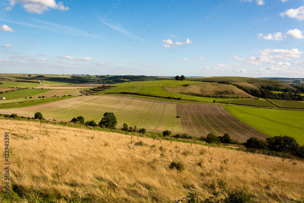 Farmer sowing seeds on field in Wiltshire, England. Tractor planting crops in field, in front of Middle Hill in the Imber Range, in the British autumn