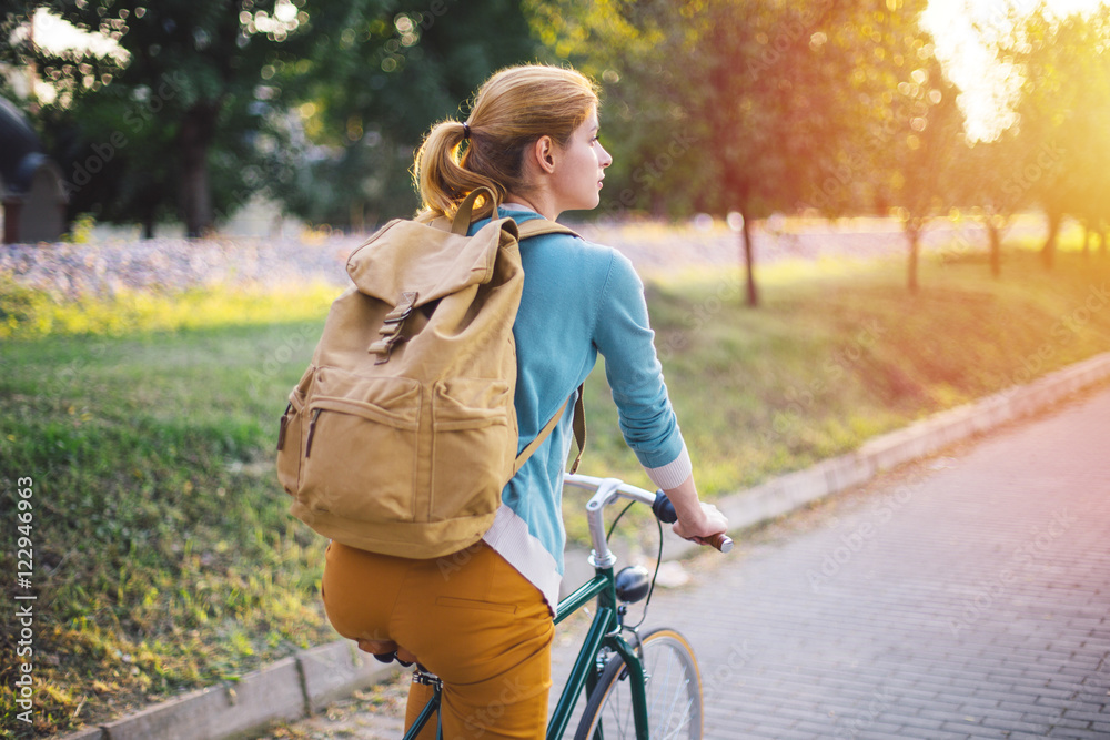 Naklejka premium Young woman with backpack cycling in the park