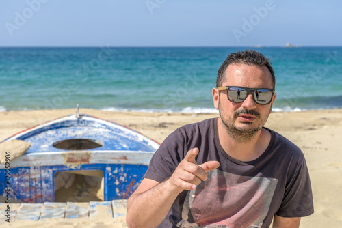 Young man on stylish outfit sitting on an abandoned fishing boat