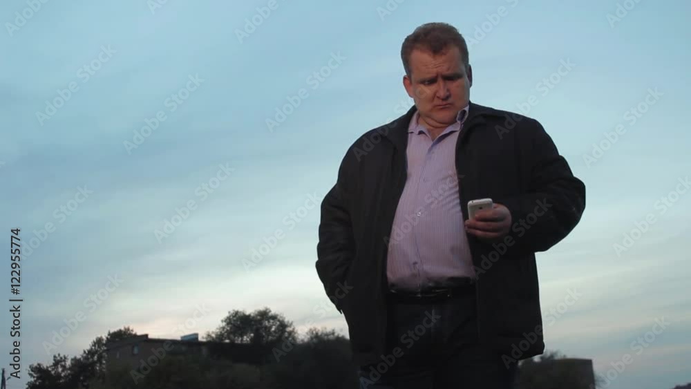Adult man reading messages on the mobile and standing at the field at the evening sky Adult man reading messages on the mobile and standing at the field at the evening sky