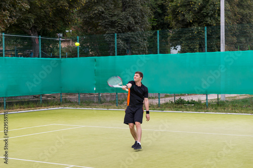 Confident young man in sports clothes playing tennis