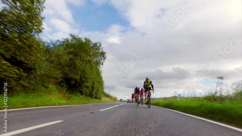 A stabilised cam of a group of cycling athletes out on a training ride on country roads in the UK countryside on a sunny day. 
