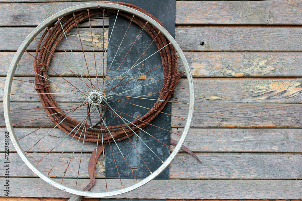 Old bike wheel and a rusty cable on a wooden wall
