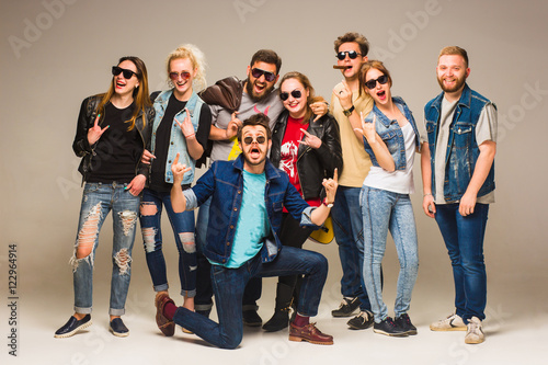 Group of happy young friends in blue jeans smiling at the camera against gray background.
