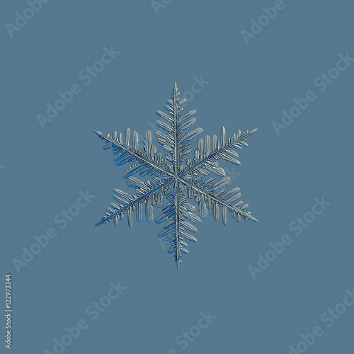 Real snowflake photo  medium size fernlike stellar dendrite   isolated on uniform blue background