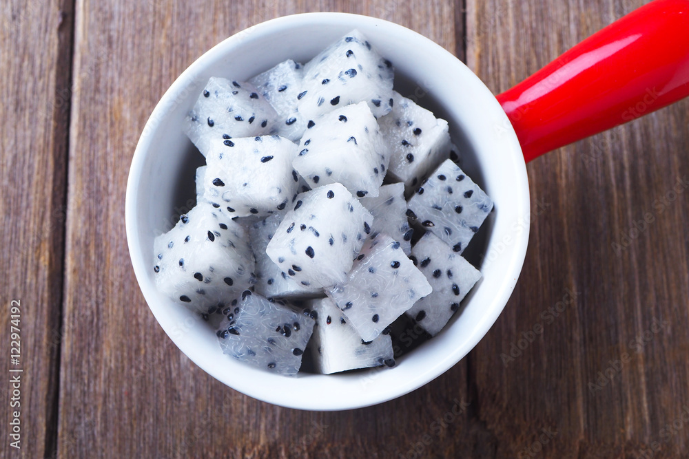 Top view of diced dragon fruit pieces in a red bowl on a wooden table