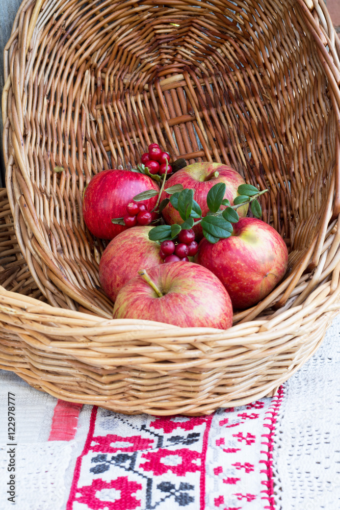На фото изображены красные спелые яблоки в плетеной тарелке