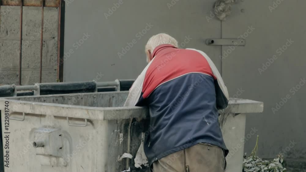 Homeless man rummaging through a dumpster. Hungry homeless man looking in garbage bins for food to eat on. Homeless man rummaging through a dumpster. Hungry homeless man looking in garbage bins for food to eat on.