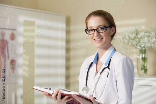 Φωτογραφία Young beautiful doctor in classes and white robe with stethoscope holding big bo