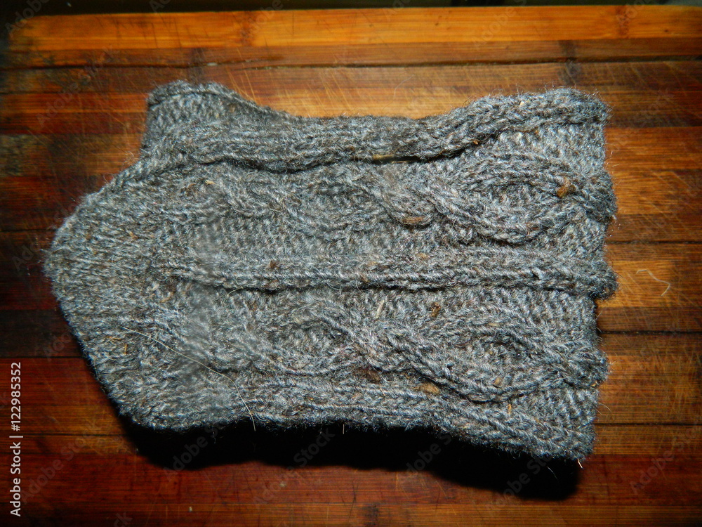 Fototapeta premium Grey knitted sock with a large pattern on a wooden board
