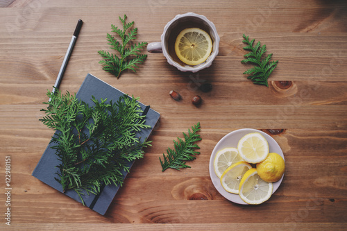 top view of notebook and pine branches with cup of tea with lemons