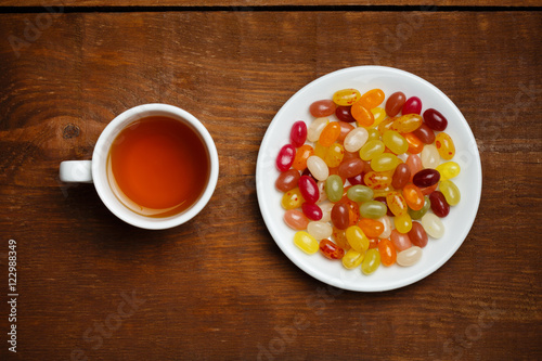 Cup of tea and plate with candies on wooden table