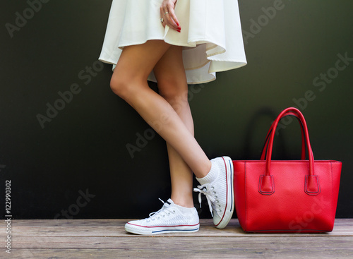 beautiful fashionable big red handbag standing next to leggy woman in white short dress and white sneakers photo