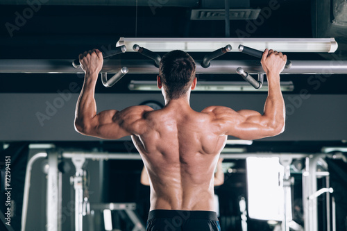 Athlete muscular fitness male model pulling up on horizontal bar in a gym