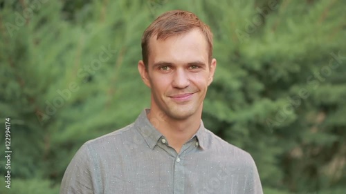 Young man smiling with yellow teeth. Vibrant green leaves as a background.