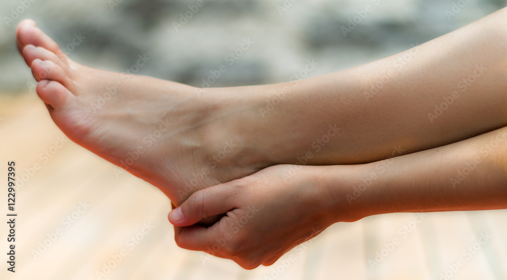 Clean woman foot and her right hand touching her heel, background of wood and stone Clean woman foot and her right hand touching her heel, background of wood and stone