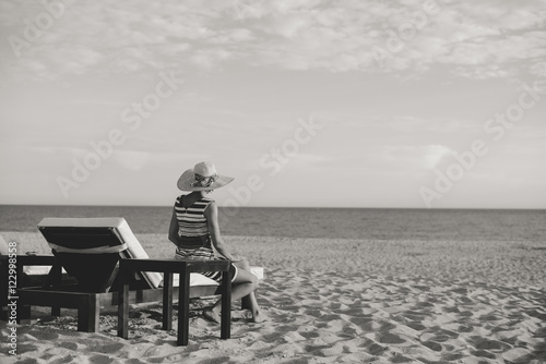 Black and white picture of woman on a tropical beach holiday. Luxury wooden lounge sunny background