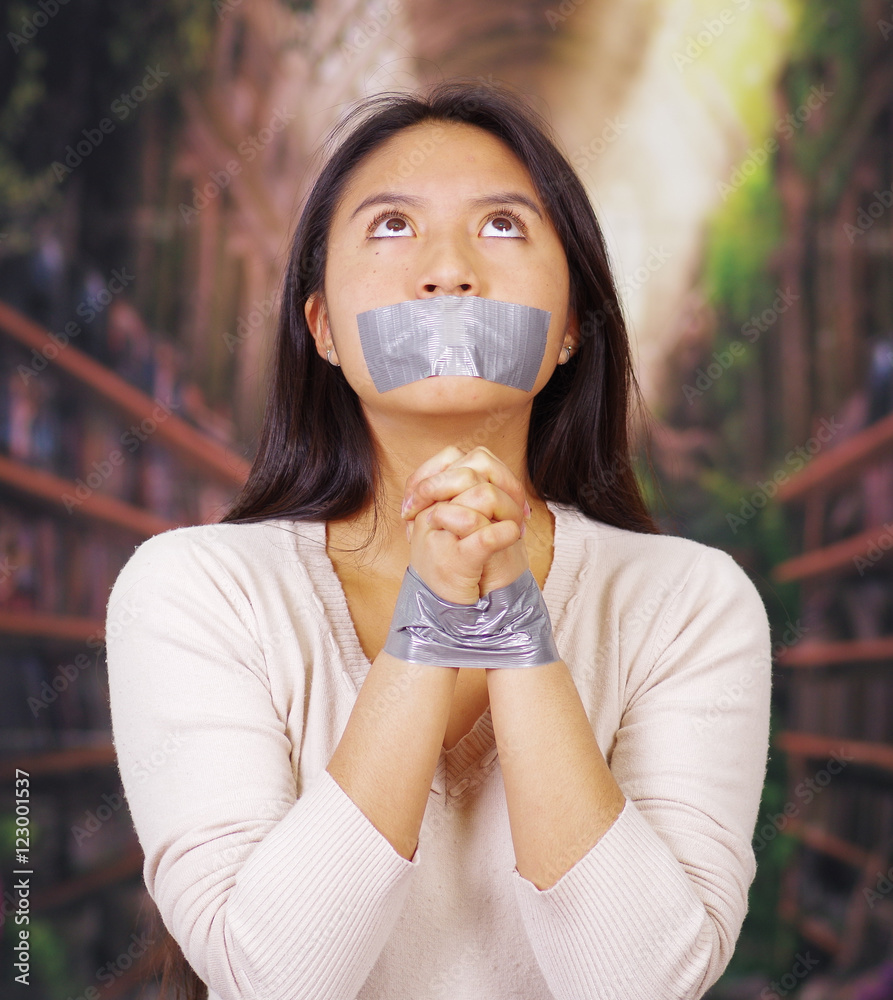 Young brunette woman wearing white sweater gagged and tied with duct tape  around wrists, facing camera, hostage concept Stock Photo | Adobe Stock