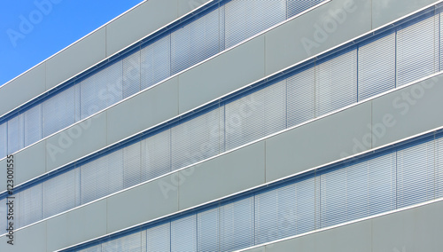 Wall of an office building with windows with closed shutters, blue sky