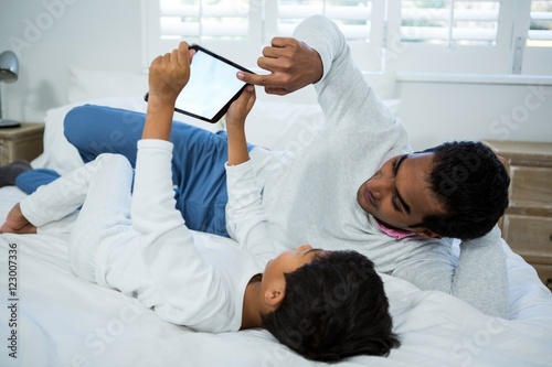 Father and son using digital tablet on bed