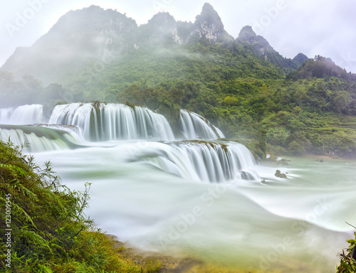 Ban Gioc Waterfall craggy limestone permissive side misty morning with grass and tones of lower cascade. It is considered most beautiful waterfalls in Southeast Asia and a national scenic Vietnam