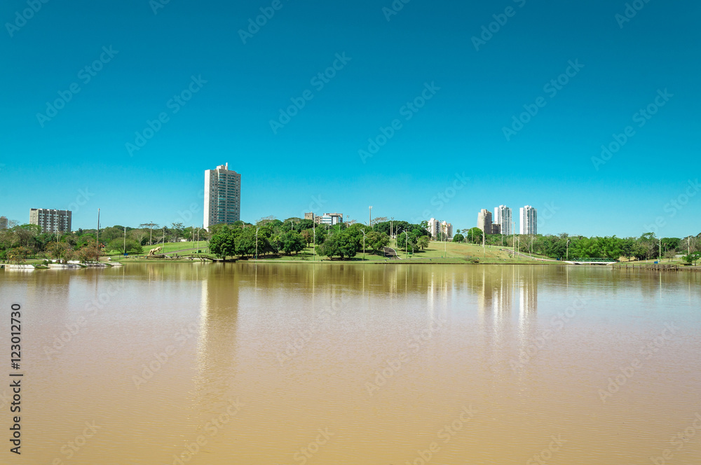 Park lake with vegetation, trees and some buildings in the background. Beautiful sunny day with reflection in water and a blue sky gradient. South America park, to relax with this beautiful view.