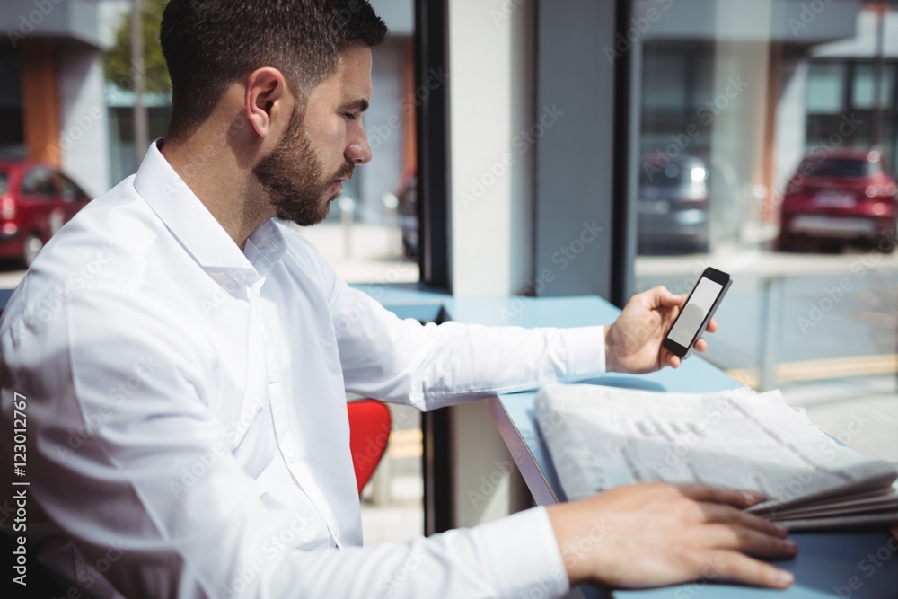 Man using mobile phone while reading newspaper Man using mobile phone while reading newspaper