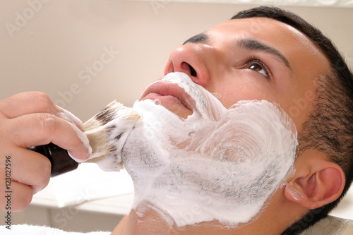 Shaving at the barber of a young boy in retro style with razor and shaving soap photo