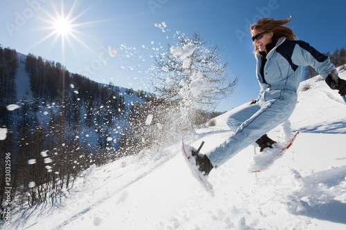 femme riant qui saute dans la neige avec des raquettes photo